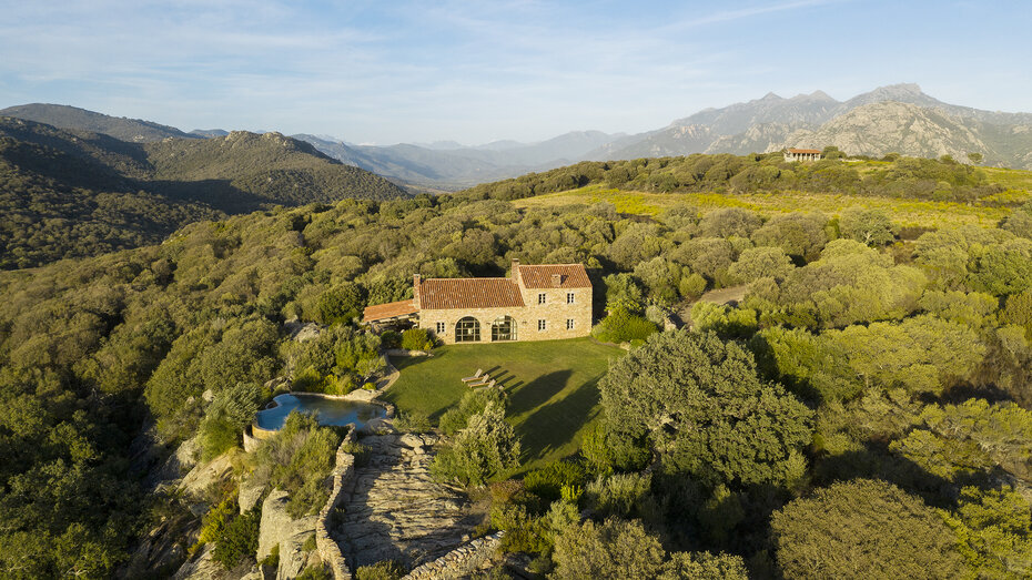 Eine grüne Hügellandschaft. Mittendrin sieht man ein altes Steinhaus mit einem kleinen Pool.