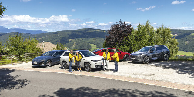 vier elektroautos stehend auf parkplatz dazwischen vier personen 
