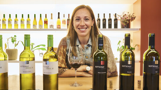 Hinter den Weinflaschen lächelt die Winzerin Victoria Gottschuly-Grassl in die Kamera.