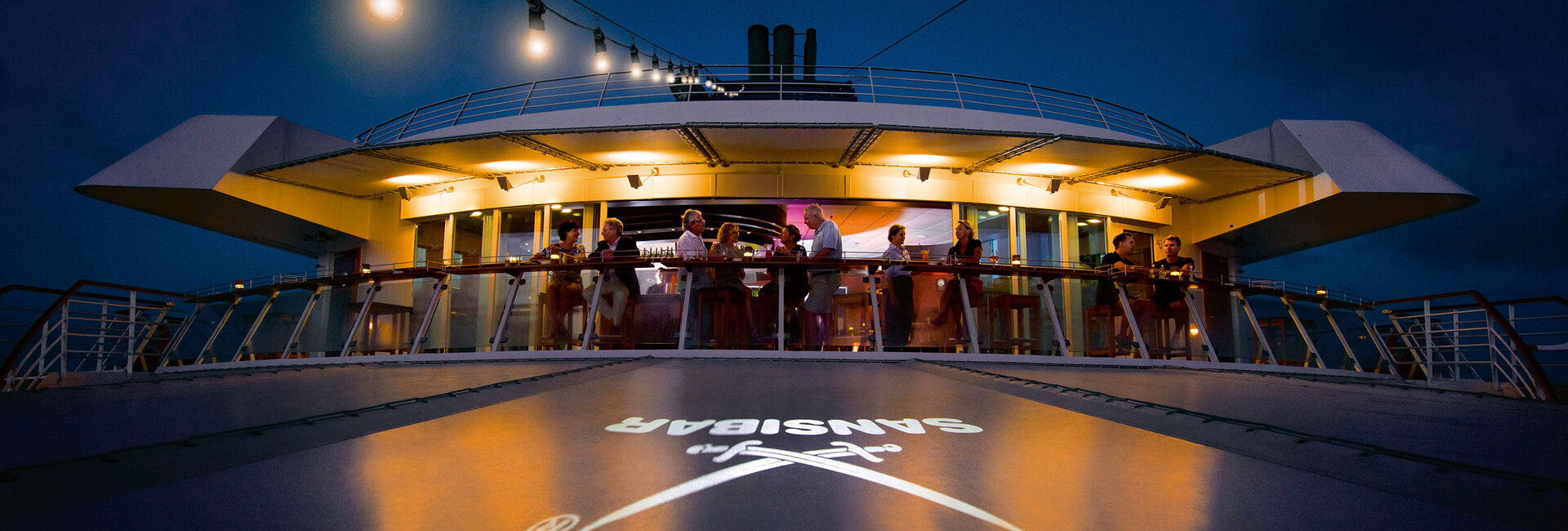 Einige Menschen stehen in der Nacht an Deck der Bar "Sansibar" auf der MS Europa und genießen den Abend.