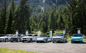 Sechs Elektroautos laden an sechs Schnellladern auf einem Parkplatz mit Bäumen im Hintergrund.