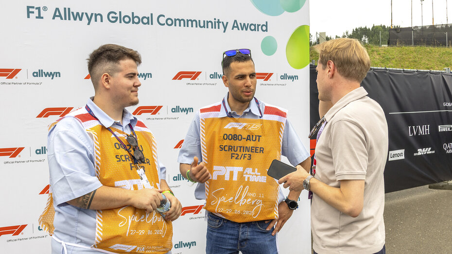 Ein Journalist spricht mit zwei technischen Kommissaren vor einer weißen Interviewwand.