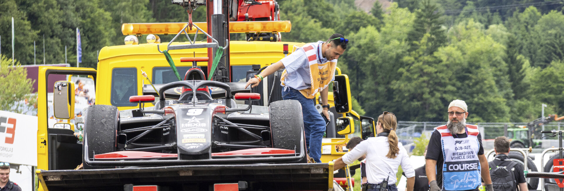 Ein Formel-Auto wird auf einem Lkw abgeschleppt, auf dem sich auch ein technischer Kommissar befindet.