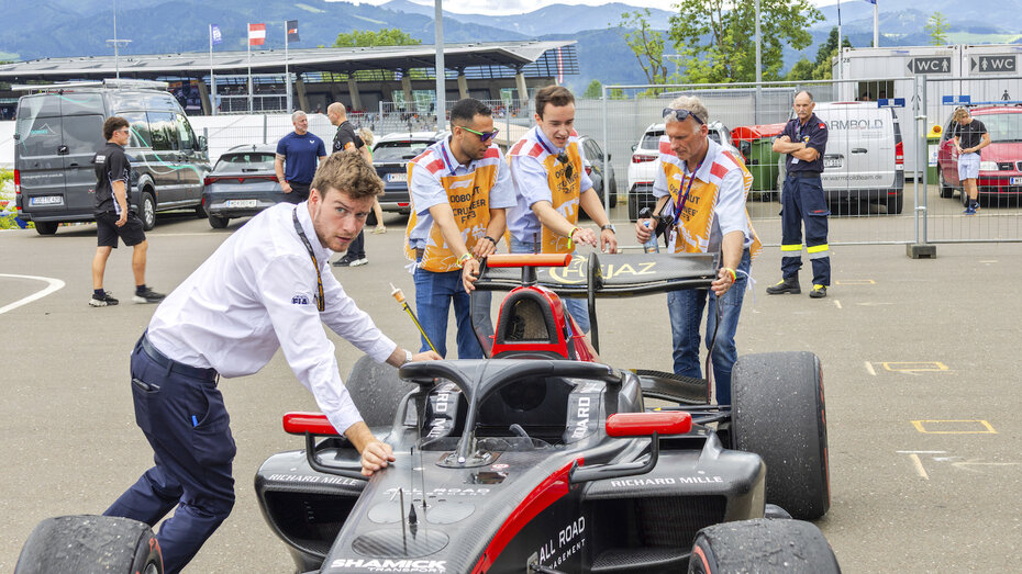 Vier Personen schieben einen schwarzen Formel-Rennwagen.
