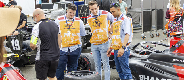 Drei Personen stehen um einen schwarzen Formel-Rennwagen.
