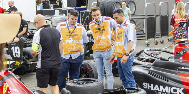 Drei Personen stehen um einen schwarzen Formel-Rennwagen.