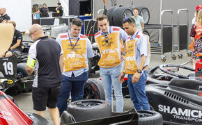 Drei Personen stehen um einen schwarzen Formel-Rennwagen.