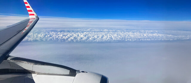 Blick auf den Himmel vom Flugzeug aus. Man sieht leicht die Tragfläche.