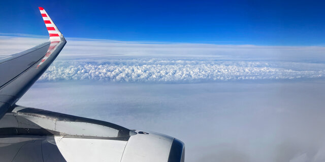 Blick auf den Himmel vom Flugzeug aus. Man sieht leicht die Tragfläche.