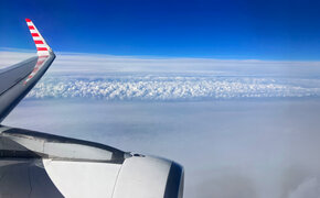 Blick auf den Himmel vom Flugzeug aus. Man sieht leicht die Tragfläche.