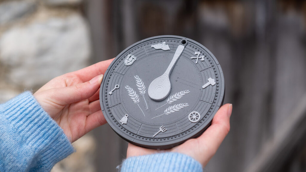 Zwei Hände halten eine dunkle runde Platte in der Hand, die aussieht wie eine Uhr, nur mit eigenartigen Schriftzeichen.