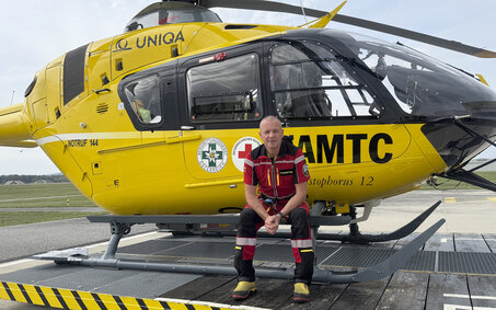 Flugretter Markus Amon sitzt in seiner Uniform vor einem Christophorus Helikopter.