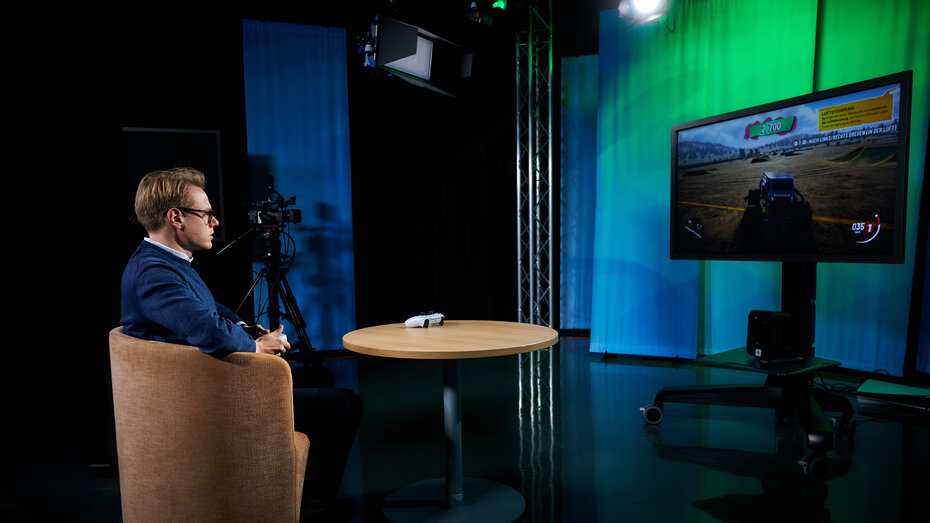 Redakteur Maximilian Barcelli sitzt mit Controller vor Bildschirm, er spielt ein Spiel.