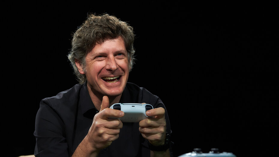 Redakteur Alex Fischer sitzt mit PS5 Controller und spielt. Er lacht. 