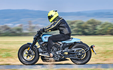 Seitlich fotografiertes, fahrendes, blau-schwarzes Motorrad. 