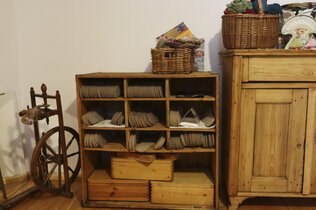 Regal, gefüllt mit Schuheinlagen aus Alpakawolle, ein Spinnrad und ein Kasten.