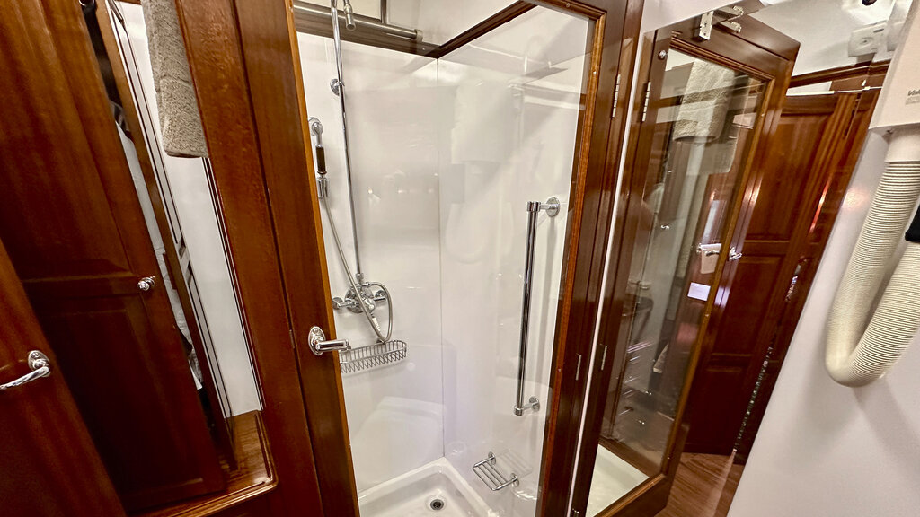 Eine Duschkabine mit gläserner Tür, daneben hängt ein Fön an der Wand.