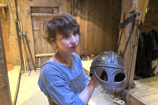 Eine Fremdenführerin zeigt einen Helm im Langhaus der Nordmänner.