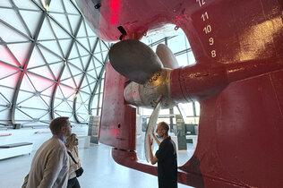 Museum: Drei Menschen stehen bei der großen Schiffsschraube.