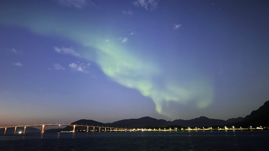 Grün schimmerndes Nordlicht über dem Meer und einer Brücke. 