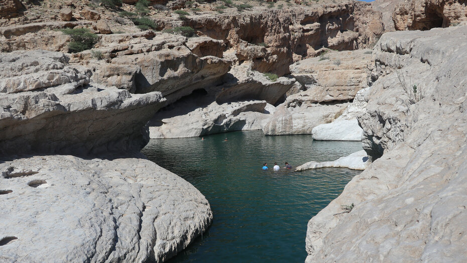 Drei Leute baden zwischen den Felsen im Oman.