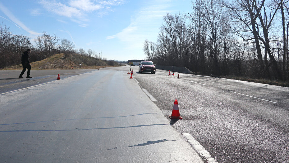Straße mit unterschiedlichem Belag und Verkehrshütchen. Ein Fahrtechnik-Instruktor steht links und beobachtet das rote Auto auf der Strecke.