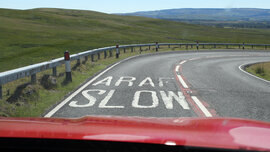 Foto zeigt (aus dem Auto fotografiert) den Straßen-Hinweis auf dem Asphalt "slow" (und auf walisisch "araf")
