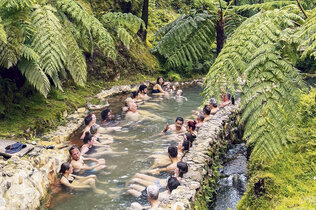 Menschen sitzen in Badekleidung im Dschungel in einer heißen Quelle.