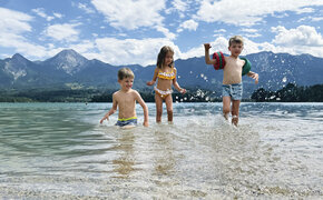 Drei kleine Kinder planschen im See, im Hintergrund die Bergkulisse.