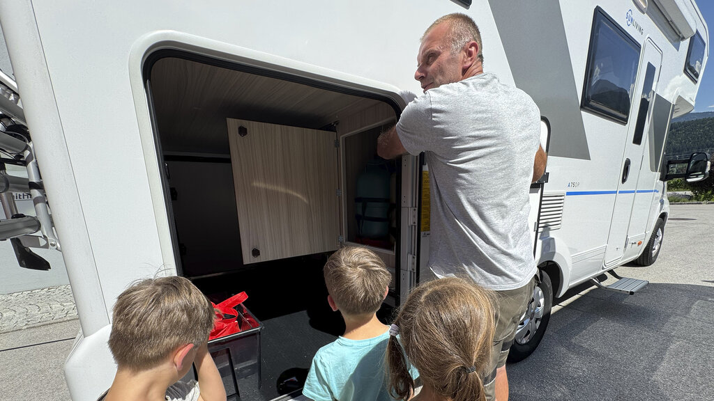 Einschulung: Der Spezialist erklärt den Bereich in der Heckgarage. 3 Kleinkinder schauen zu.