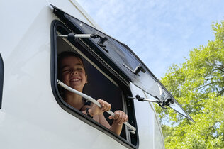 Ein Kind lacht aus dem Wohnwagen-Fenster.