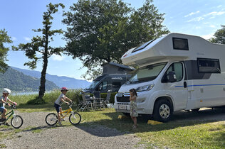 Kinder fahren am Campingplatz vor ihrem Wohnmobil mit ihrem Rad.