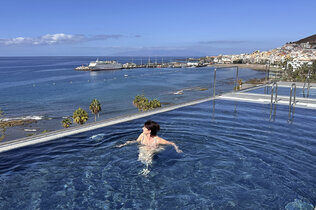 Eine Frau schwimmt im Dachpool eines Hotels und blickt auf Hafen und Meer.