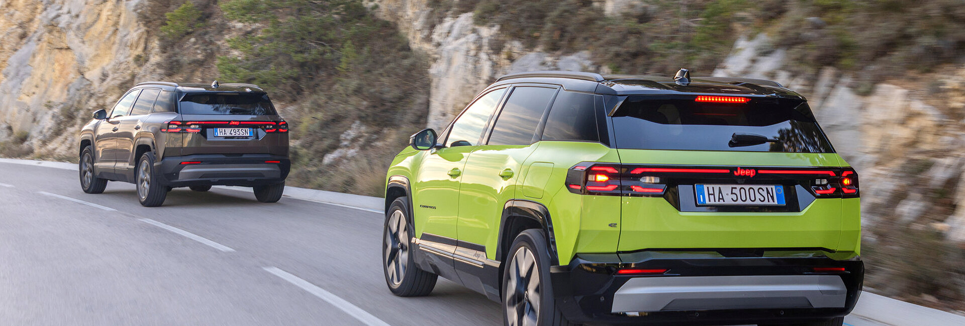 Ein grauer und ein grüner Jeep Compass fahren auf einer Landstraße an einer Felswand vorbei.