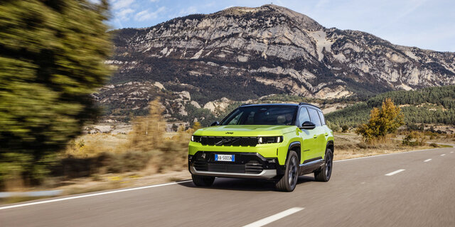 Ein grüner Jeep Compass fährt über eine Landstraße mit Hügeln im Hintergrund.