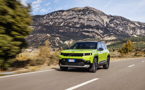 Ein grüner Jeep Compass fährt über eine Landstraße mit Hügeln im Hintergrund.