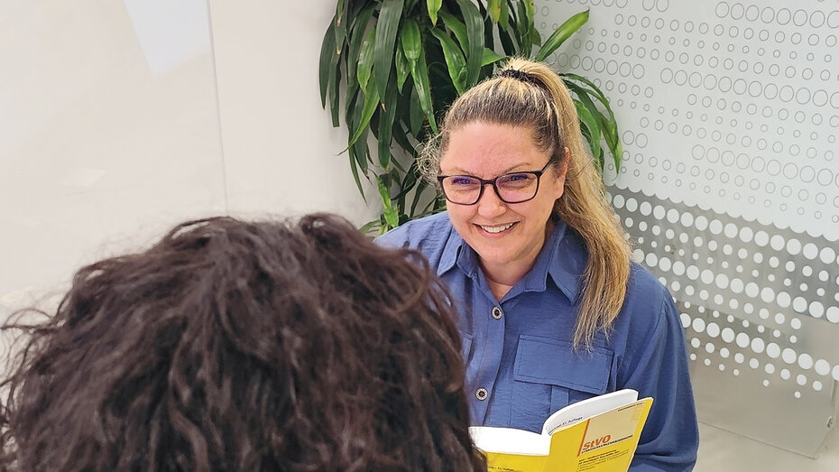 ÖAMTC Juristin, sie sitzt auf ihrem Arbeitsplatz und spricht mit einem Mitglied. Sie hat einen blonden Pferdeschwanz und eine Brille.