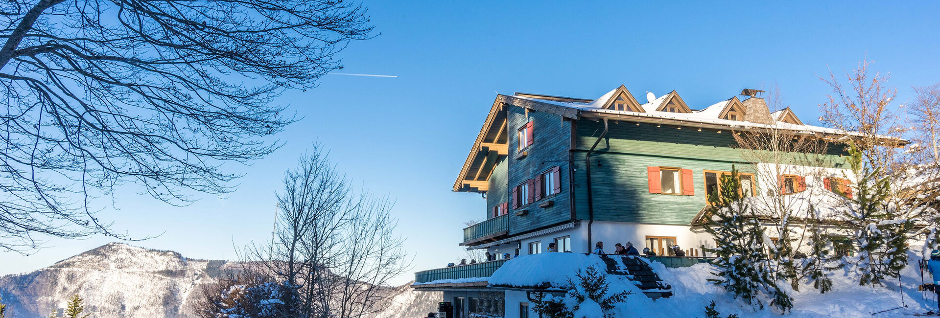 Das Hotel Hochberghaus am Kasberg umgeben von Bergen und einer Schneelandschaft.