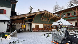 Außenaufnahme des Hotels Hochberghaus am Kasberg in Grünau im Almtal. Zu sehen sind drei Gebäude, davor liegen Ski im Schnee.
