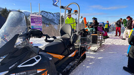 Im Vordergrund steht ein Ski-Do bei der Bergstation am Kasberg. Er ist mit einem Anhänger fürs Gepäck ausgestattet.