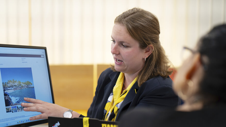 Eine Frau im Reisebüro erklärt einer anderen etwas.