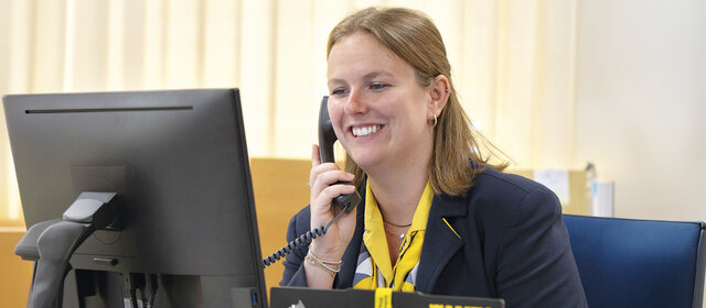 Reisebürokauffrau Katharina Wiesbauer am Telefon, wie sie auf den Computerbildschirm blickt.