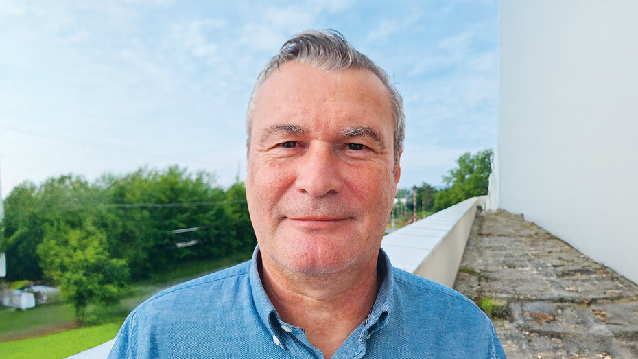 Porträtfoto eines Mannes mit grauen Haaren, er trägt ein blaues Hemd