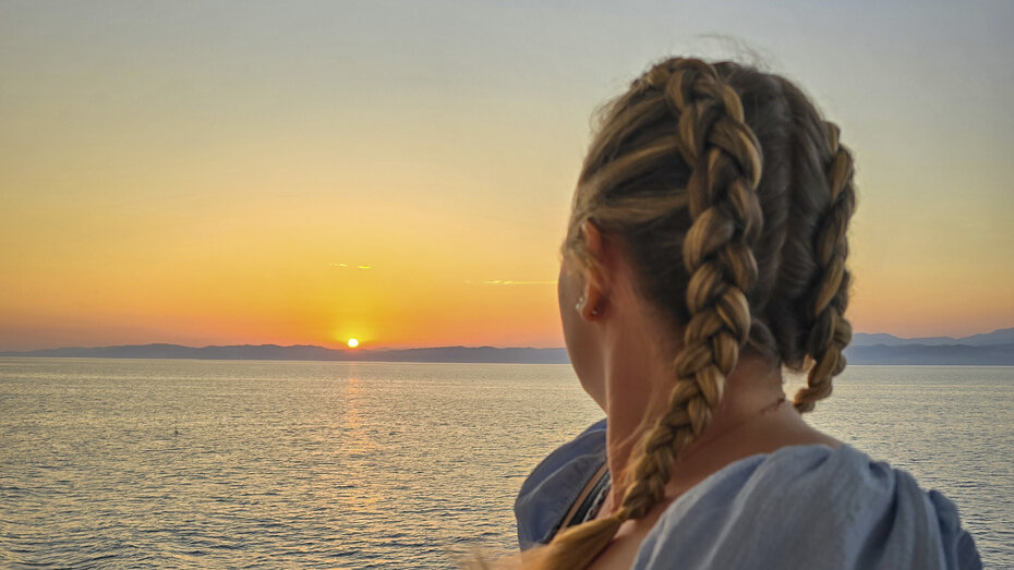 Katharina blickt aufs Meer zum Sonnenuntergang von einer Reeling aus.
