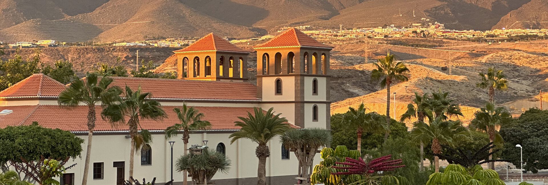 Eine Kirche mit zwei Türmen umgeben von Palmen in einer wüstenähnlichen Landschaft.