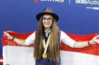 Pannenfahrerin Leonie Tieber mit Steirerhut und Medaille nach ihrem Sieg bei den Euroskills 2025. Hinter ihrem Rücken hält sie eine Österreich-Flagge.