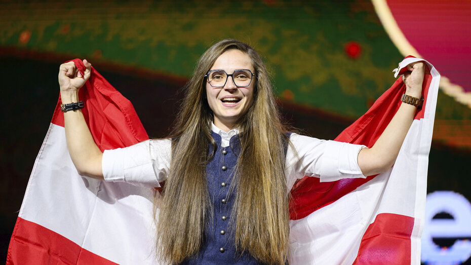 Pannenfahrerin Leonie Tieber mit einer hinter ihrem Rücken aufgebreiteten Österreich-Flagge. Sie hat lange offene Haare.