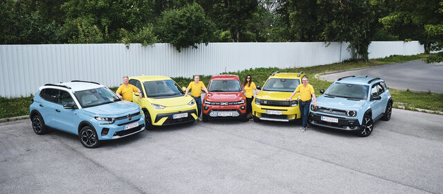 Fünf kleine Elektroautos nebeneinander aufgereiht, stehend von vorne, mit vier Personen