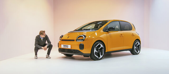 Eine Person hockt in einem Studio neben einem orangenen Renault Twingo 2025, der in einem Studio steht.