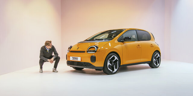 Eine Person hockt in einem Studio neben einem orangenen Renault Twingo 2025, der in einem Studio steht.